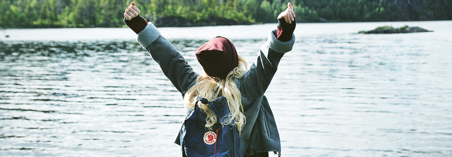 a happy person raising hands beside lake